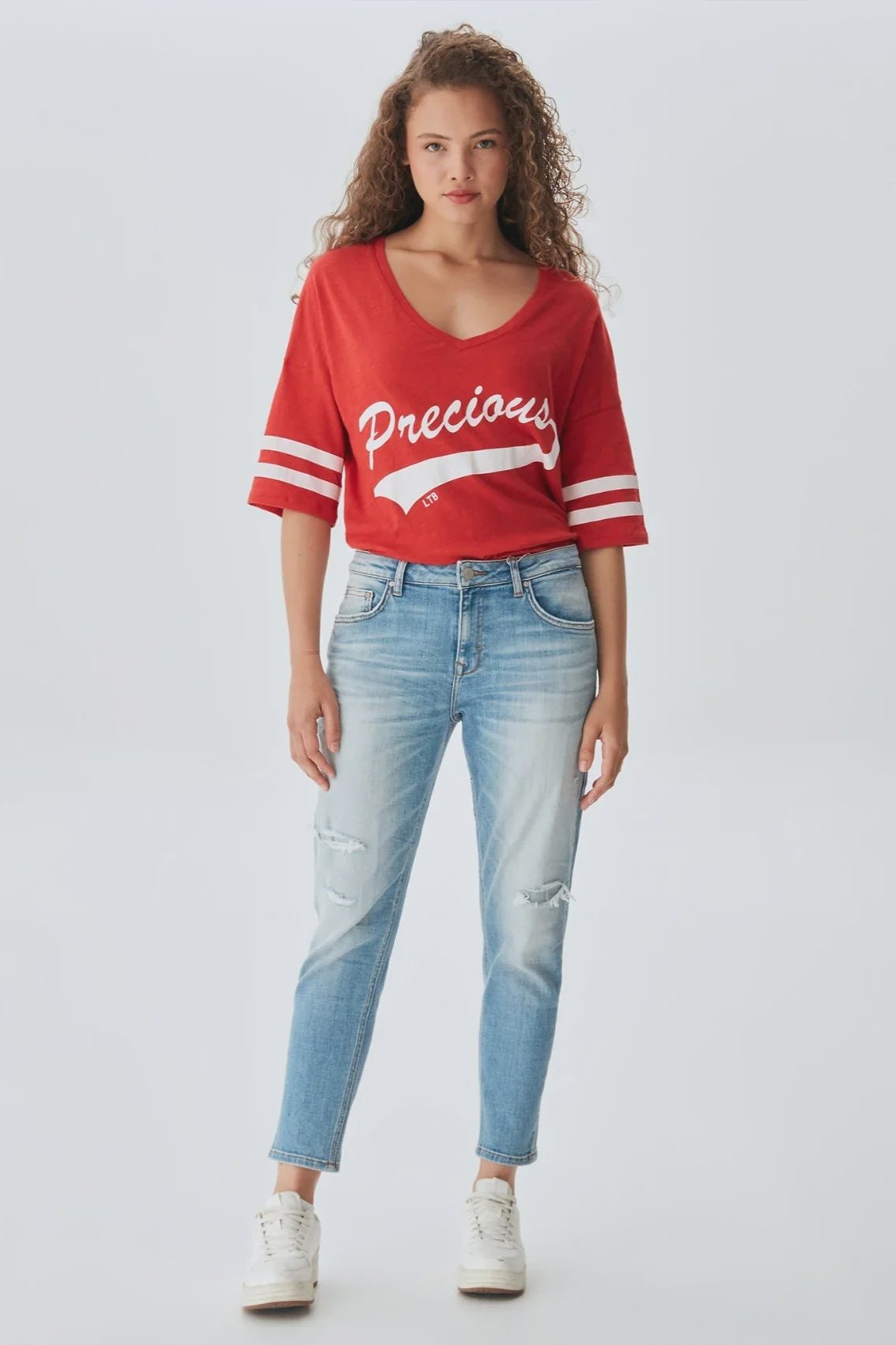 A female model wearing a red slim-fit boyfriend jean with a white and red 'PRECISION' text on the chest and blue denim jeans.