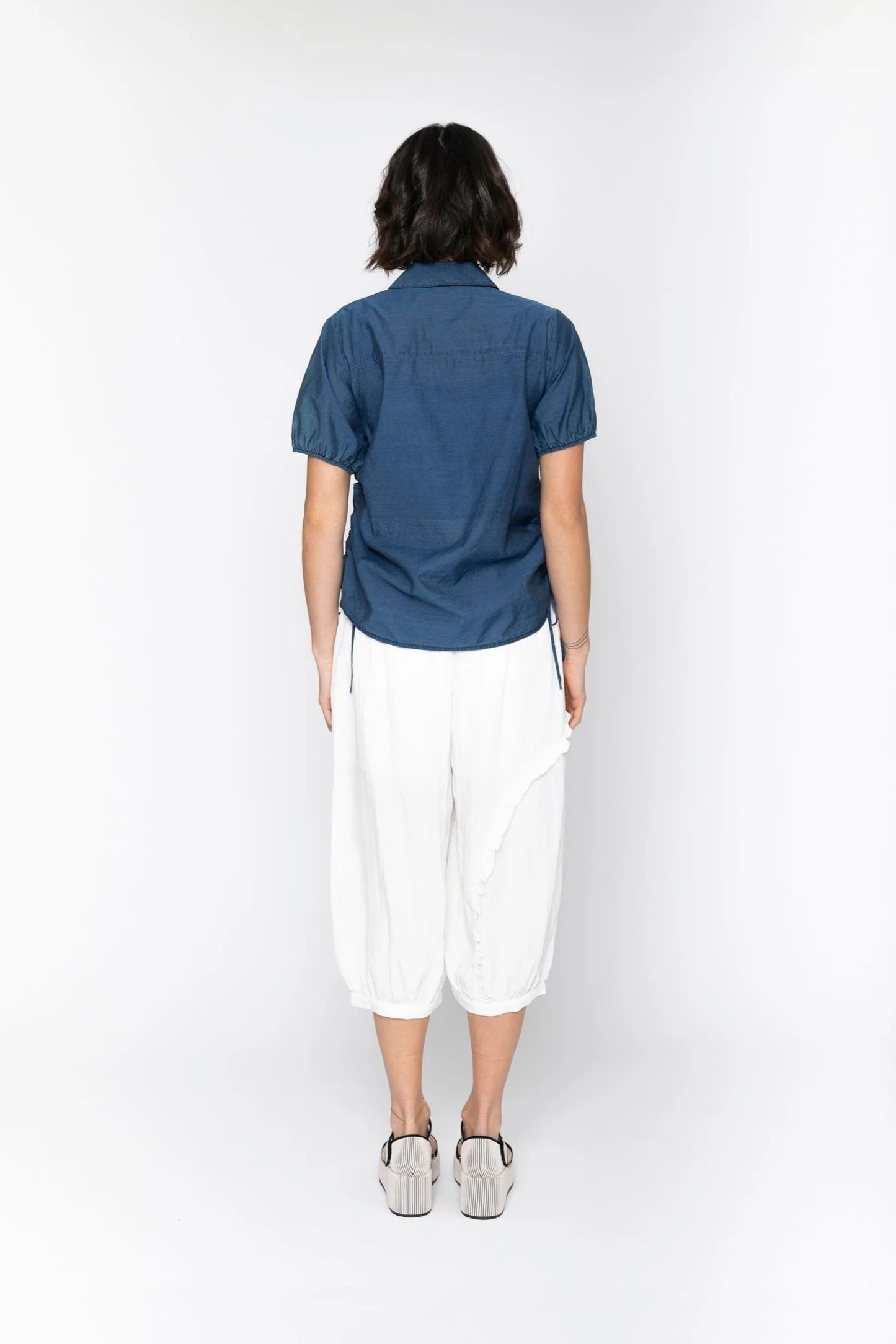 Person wearing a blue shirt and white pants on a white background