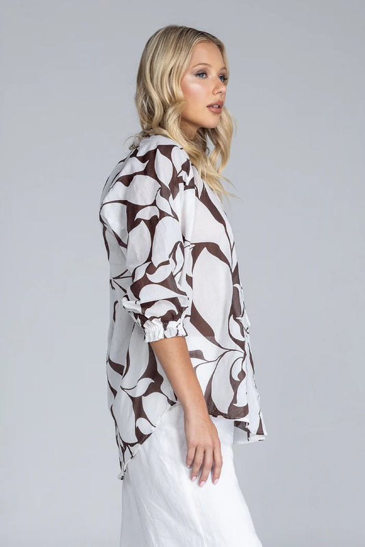 Woman wearing a patterned blouse and white pants on a gray background