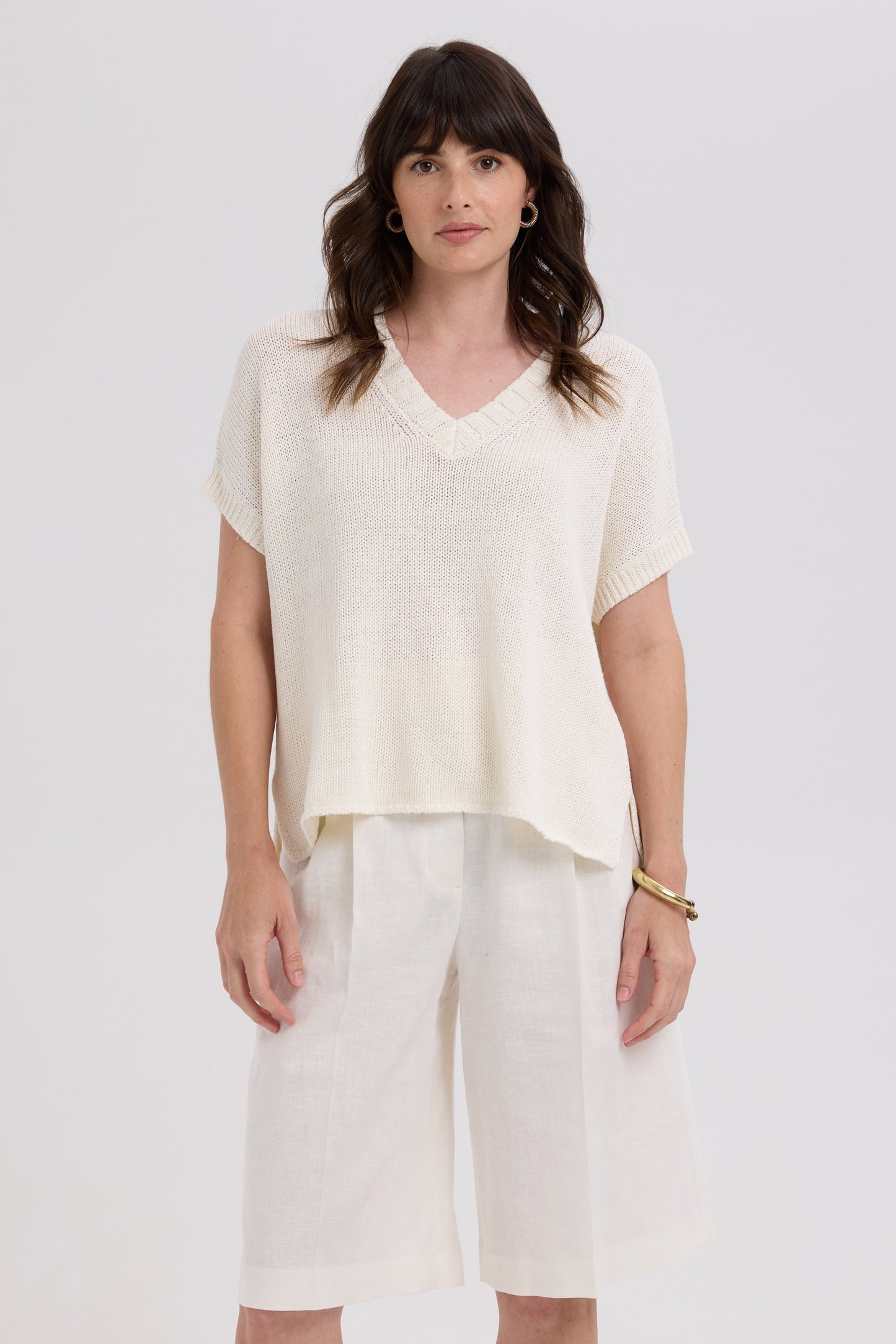 Woman wearing a white top and light-colored pants against a plain background