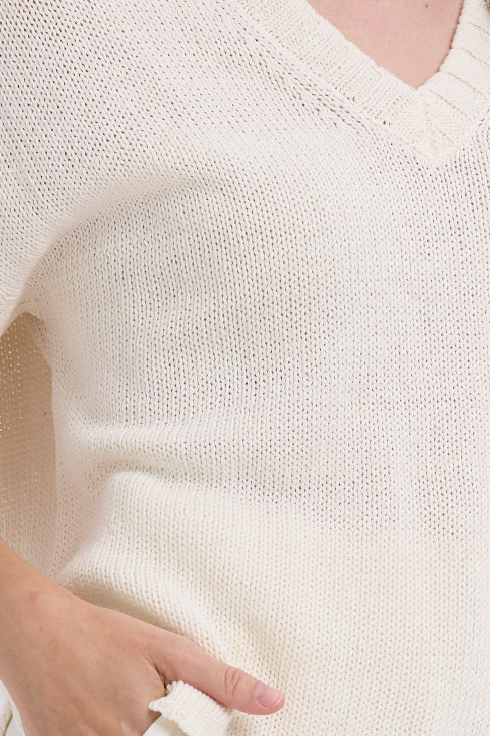 Close-up of a person wearing a white knit sweater with a hand visible.