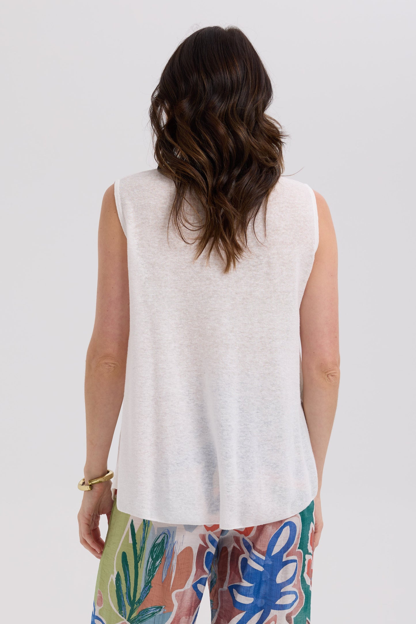 Person wearing a white sleeveless top and colorful pants on a plain background
