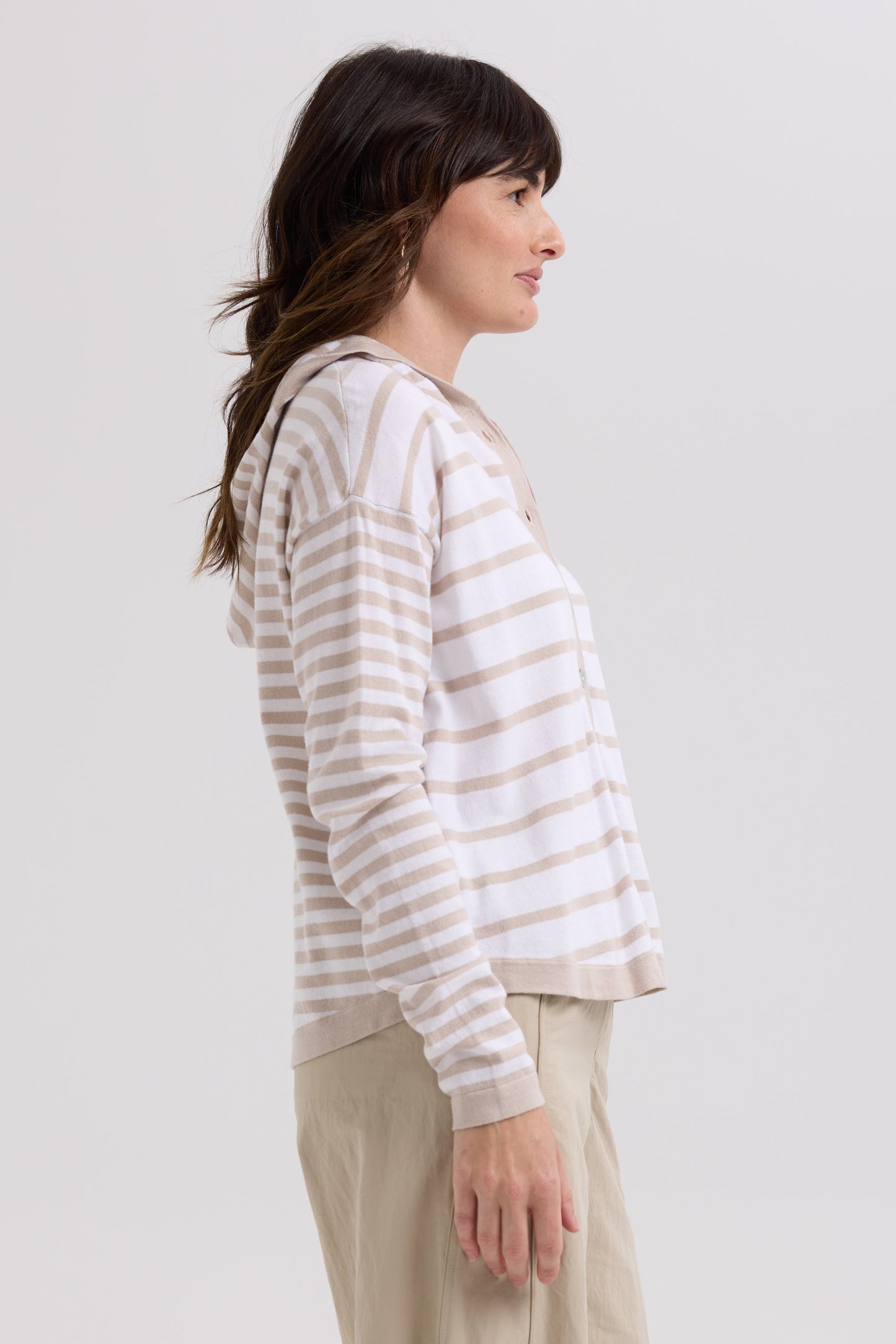 Woman wearing a striped hoodie and beige pants on a plain background
