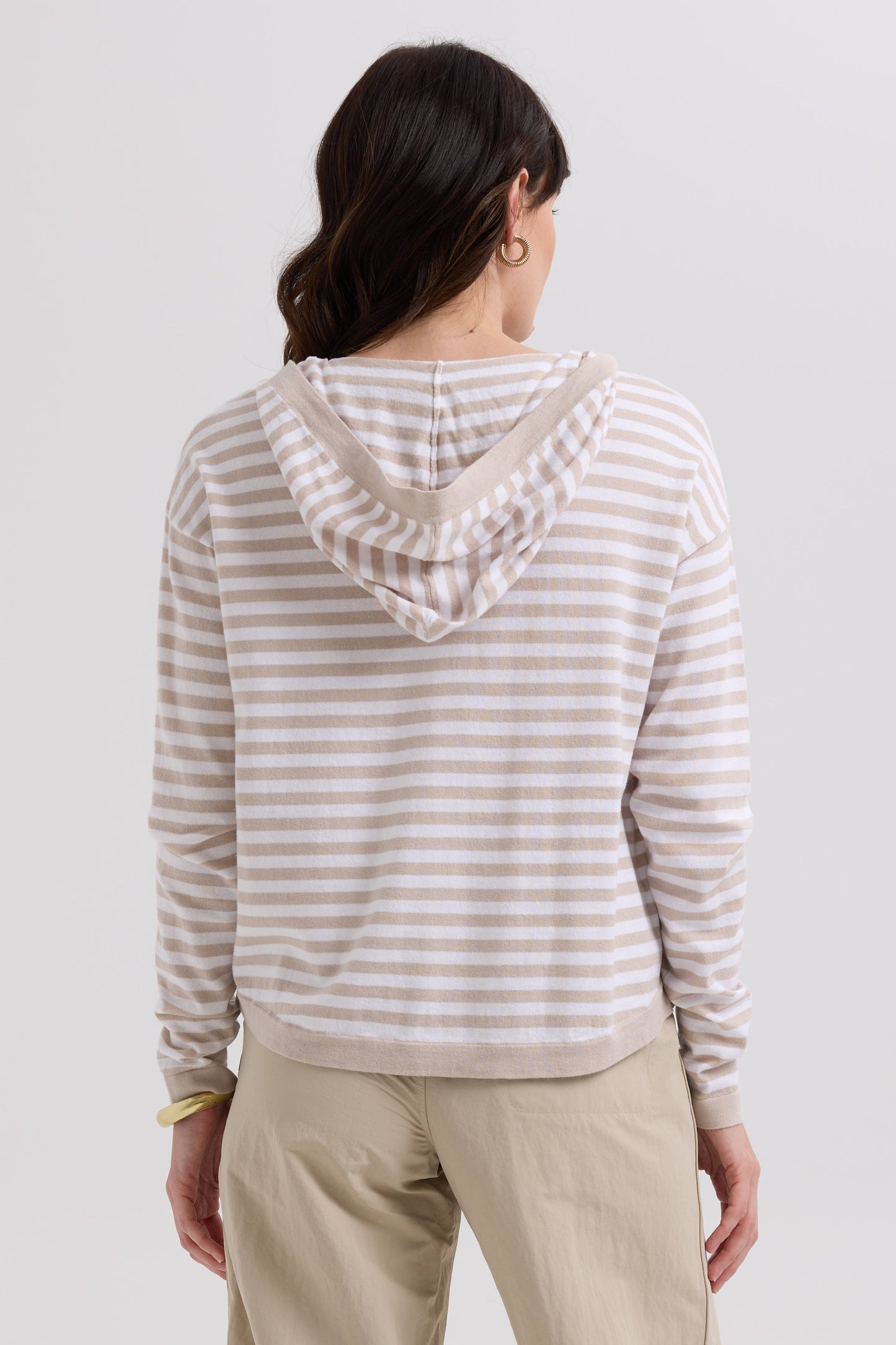 Person wearing a striped hoodie and beige pants on a plain background