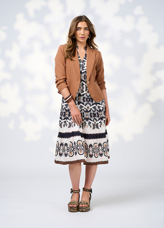 Woman wearing a patterned dress with a brown blazer against a white background