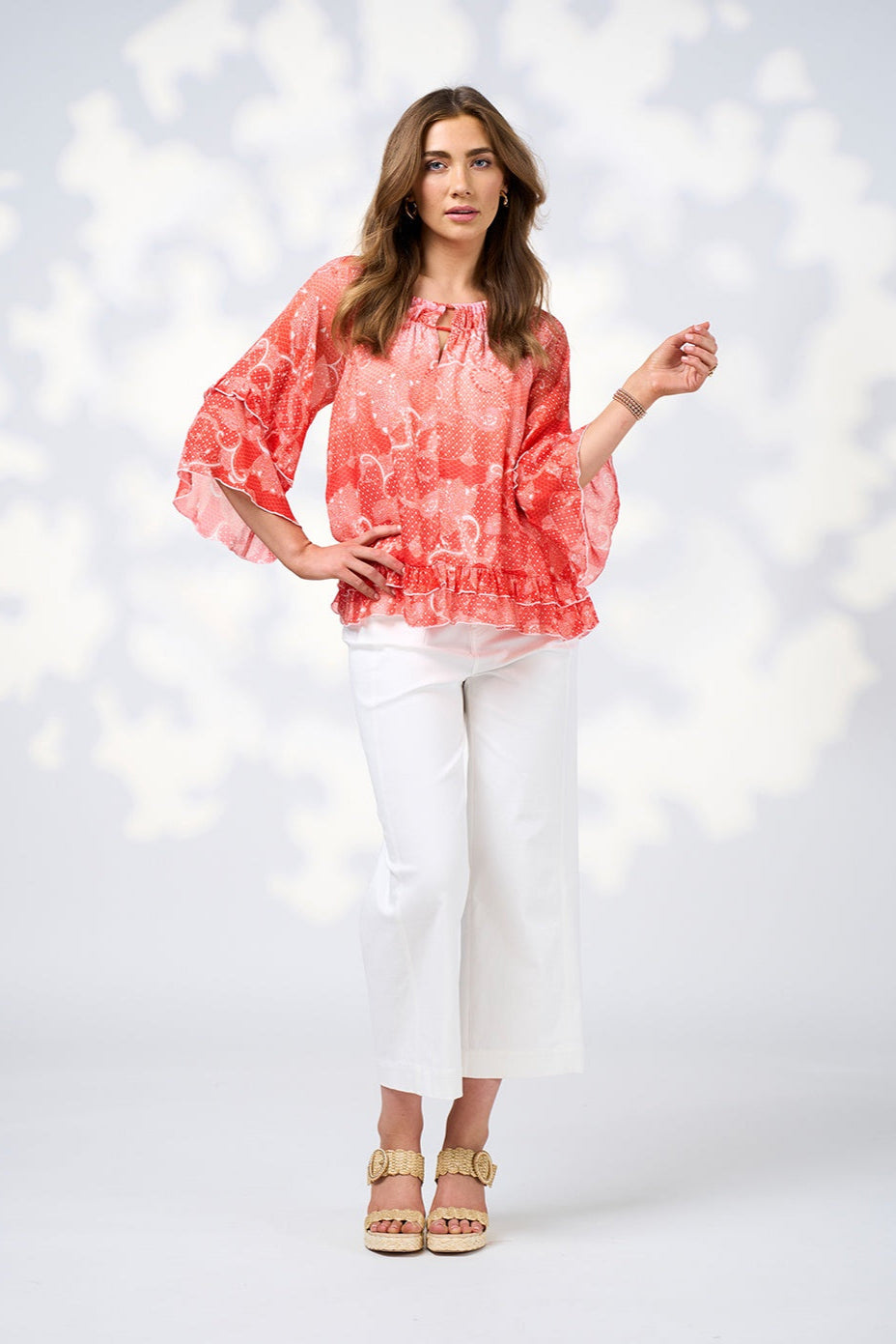 Woman wearing a coral patterned blouse and white pants against a light background