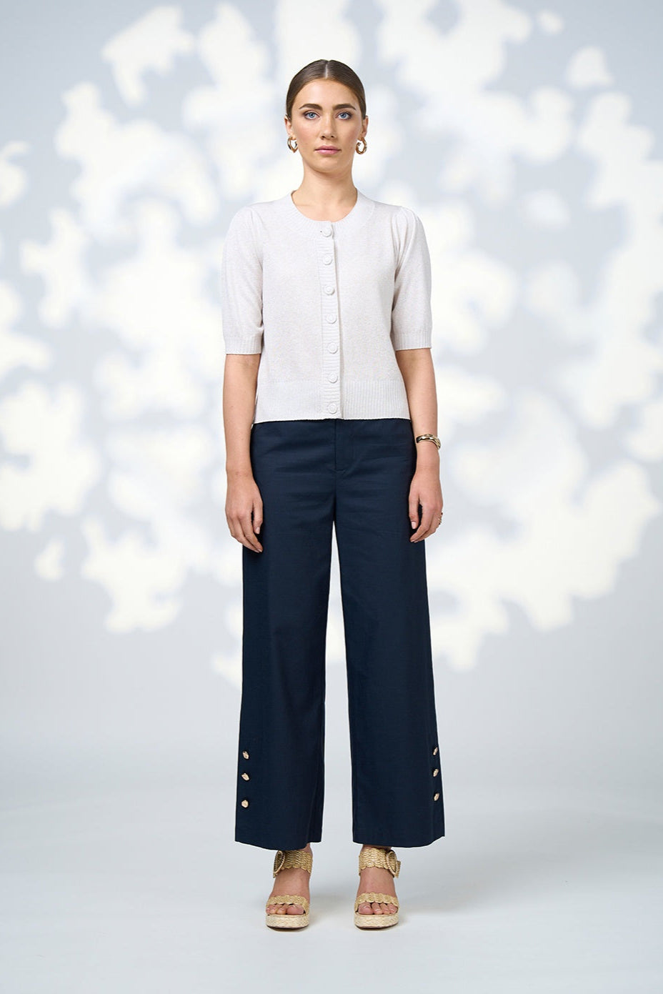 Woman wearing a white top and navy pants against a light background