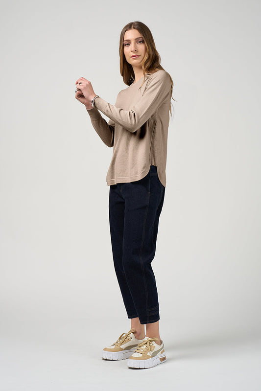 Woman wearing a beige sweater and dark pants on a white background
