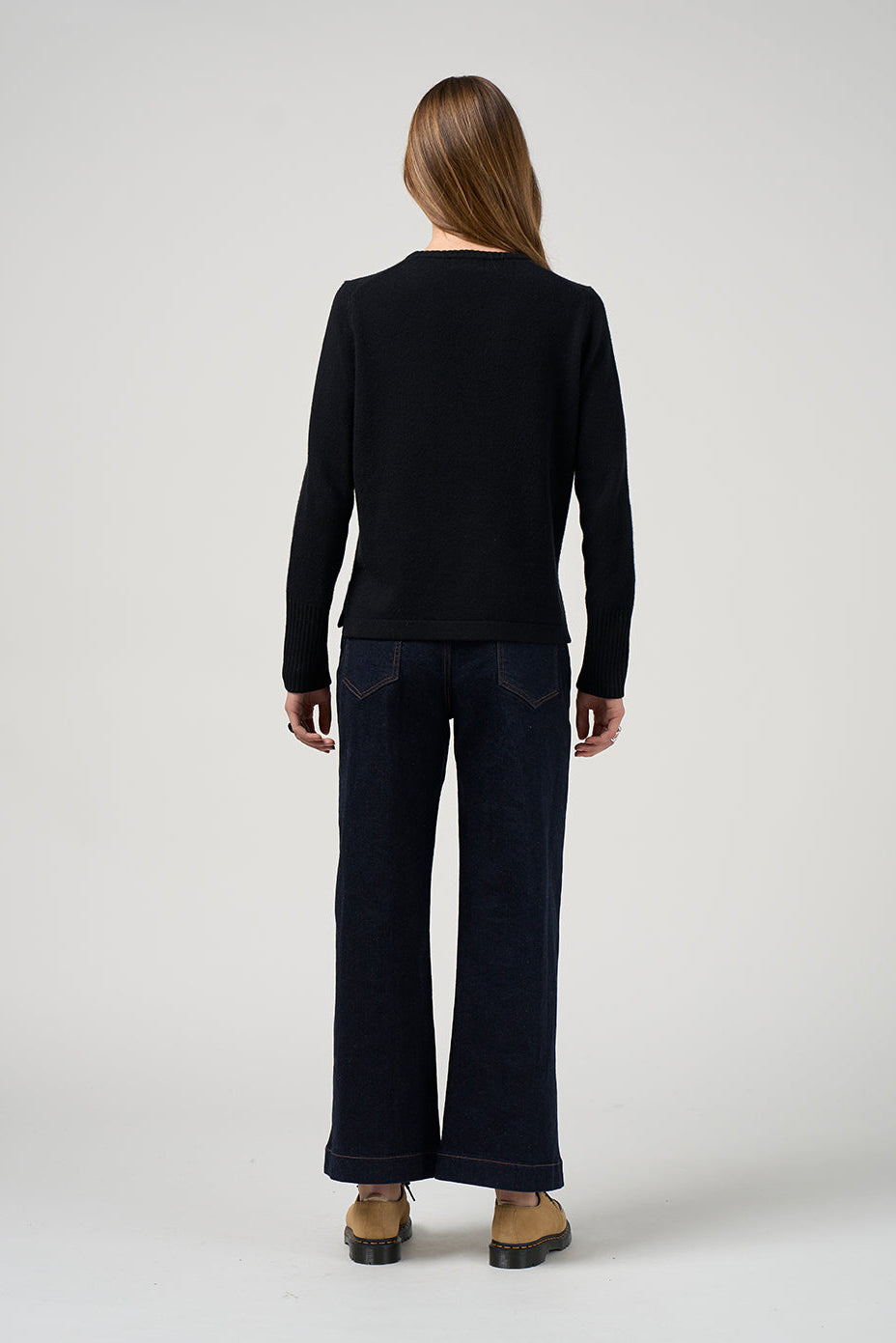 Person wearing a black long-sleeve top and dark jeans on a white background