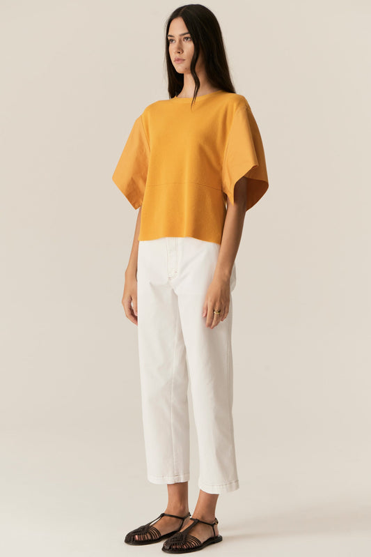 Woman wearing a mustard yellow top and white pants on a beige background