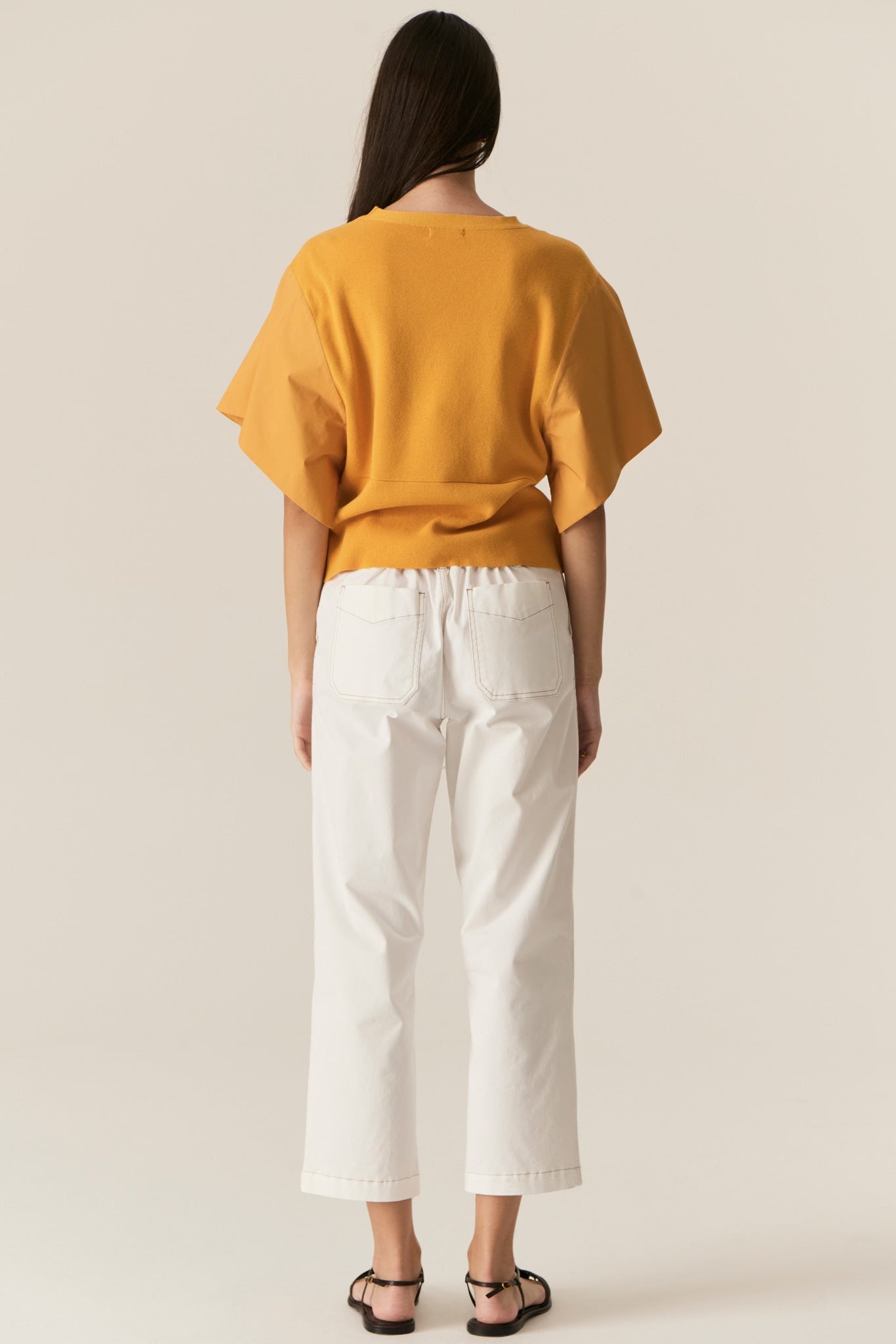 Person wearing a yellow top and white pants on a beige background