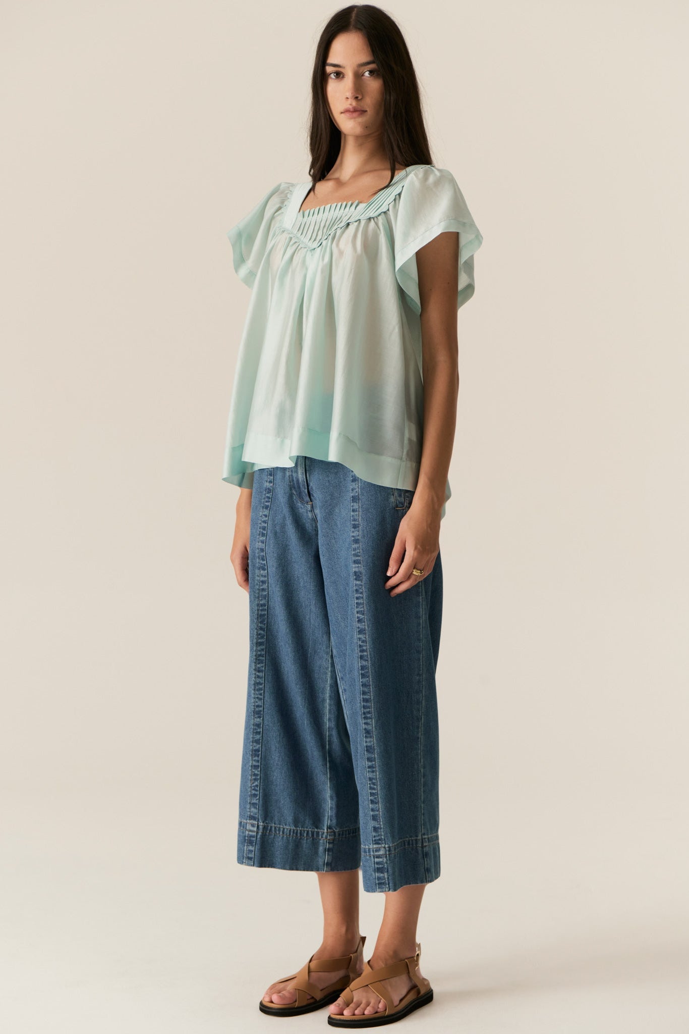 Woman wearing a light blue top and denim pants on a plain background