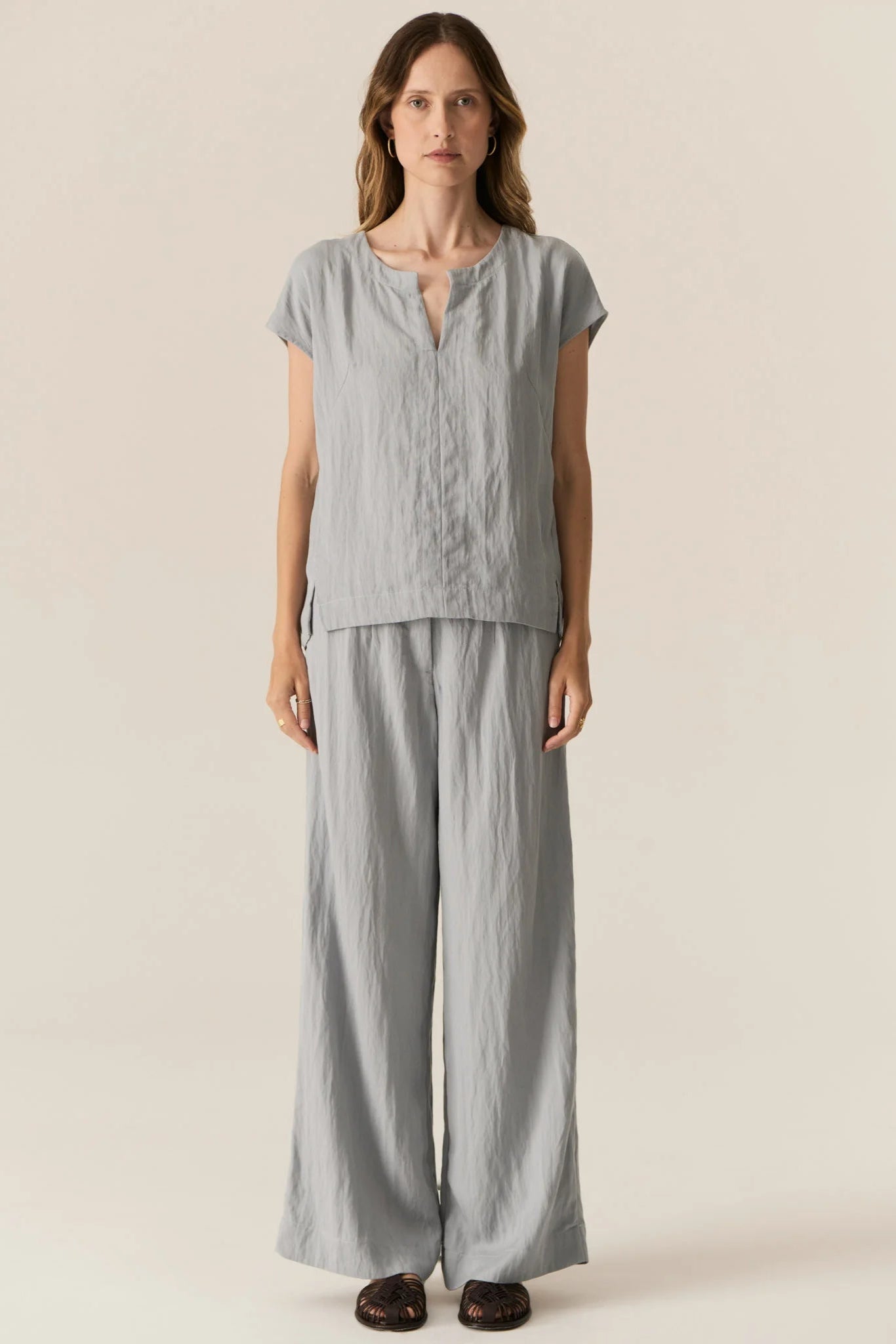 Woman wearing a light gray top and wide-leg pants on a beige background