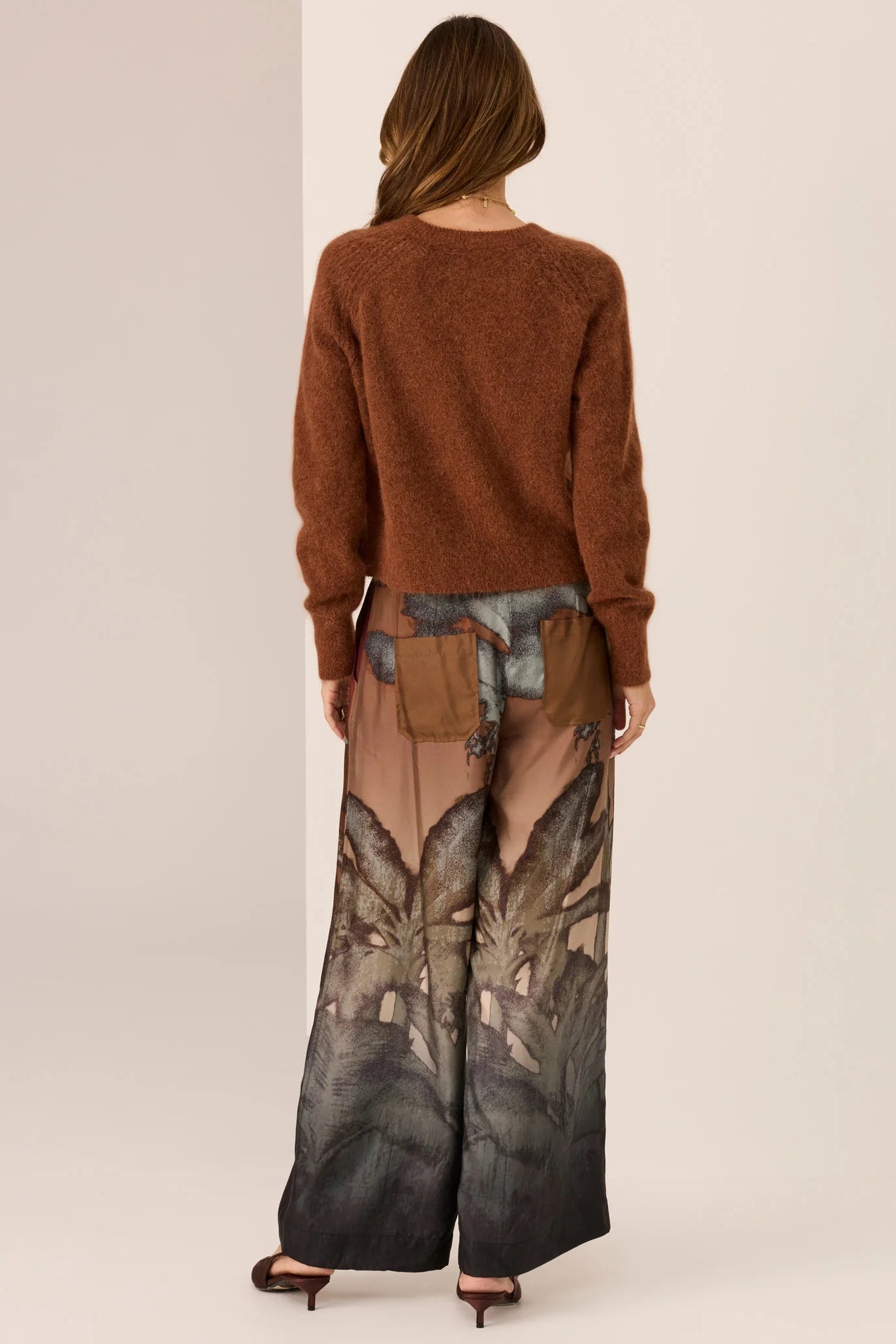 Person wearing a brown sweater and patterned pants on a plain background