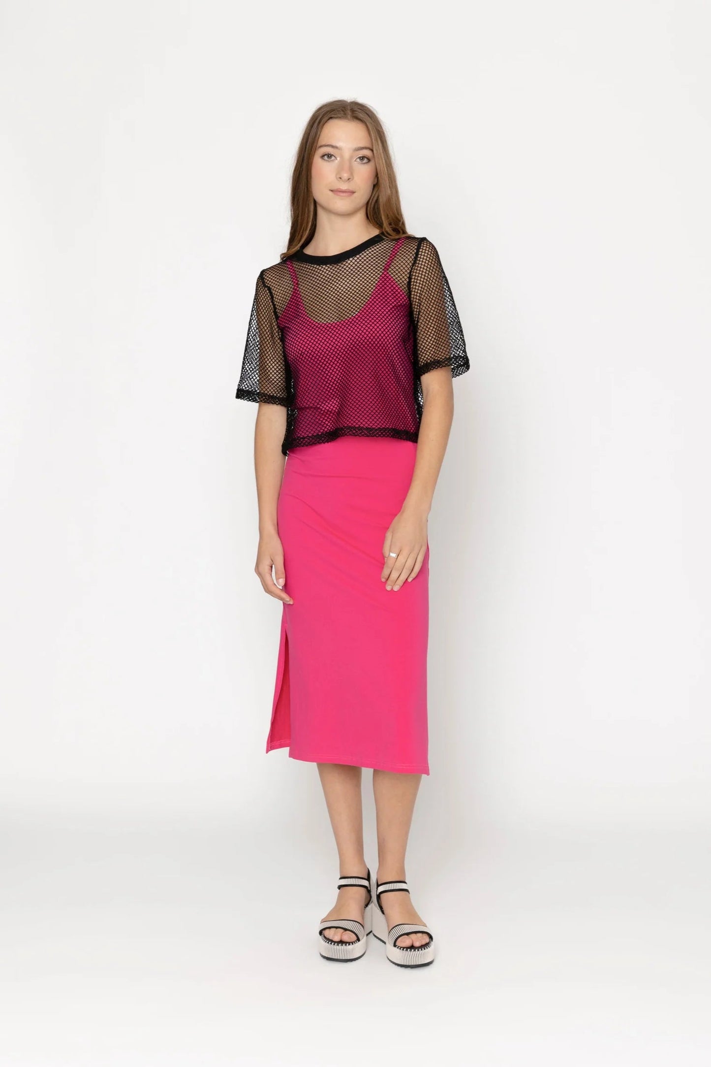 Woman wearing a pink skirt and black top with sheer sleeves on a white background