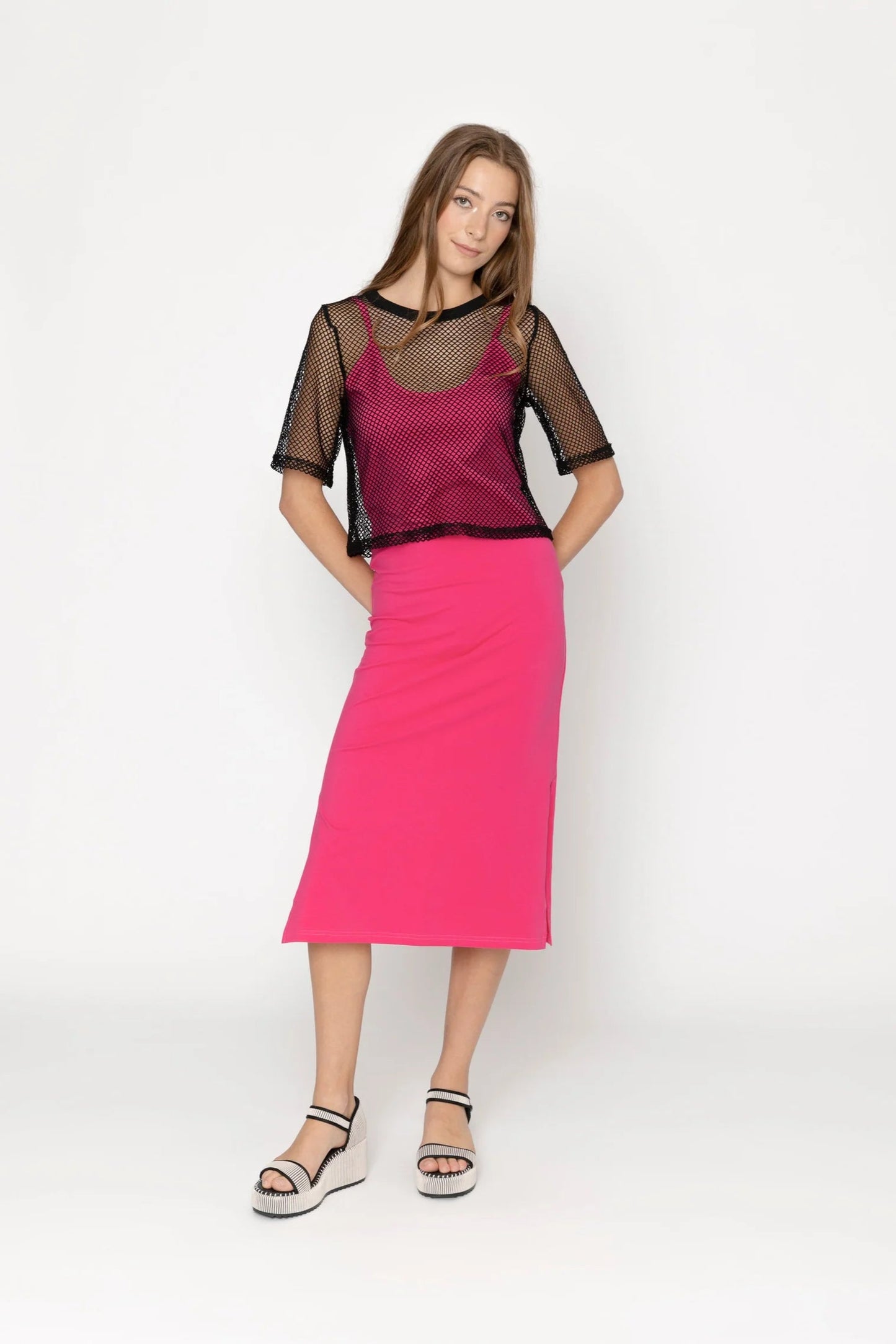 Woman wearing a pink dress with a sheer black top on a white background