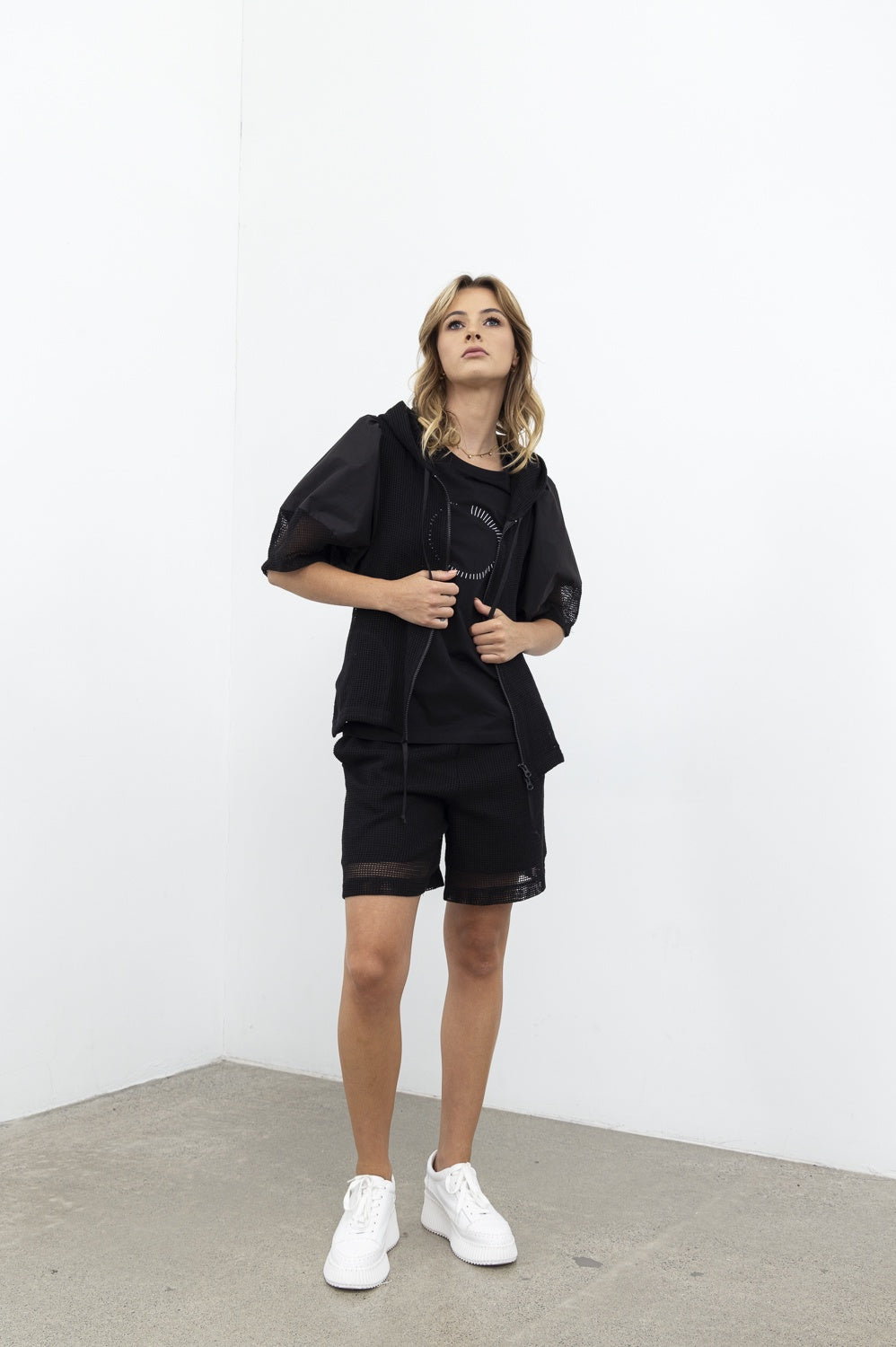 Person wearing a black outfit with white sneakers against a white background