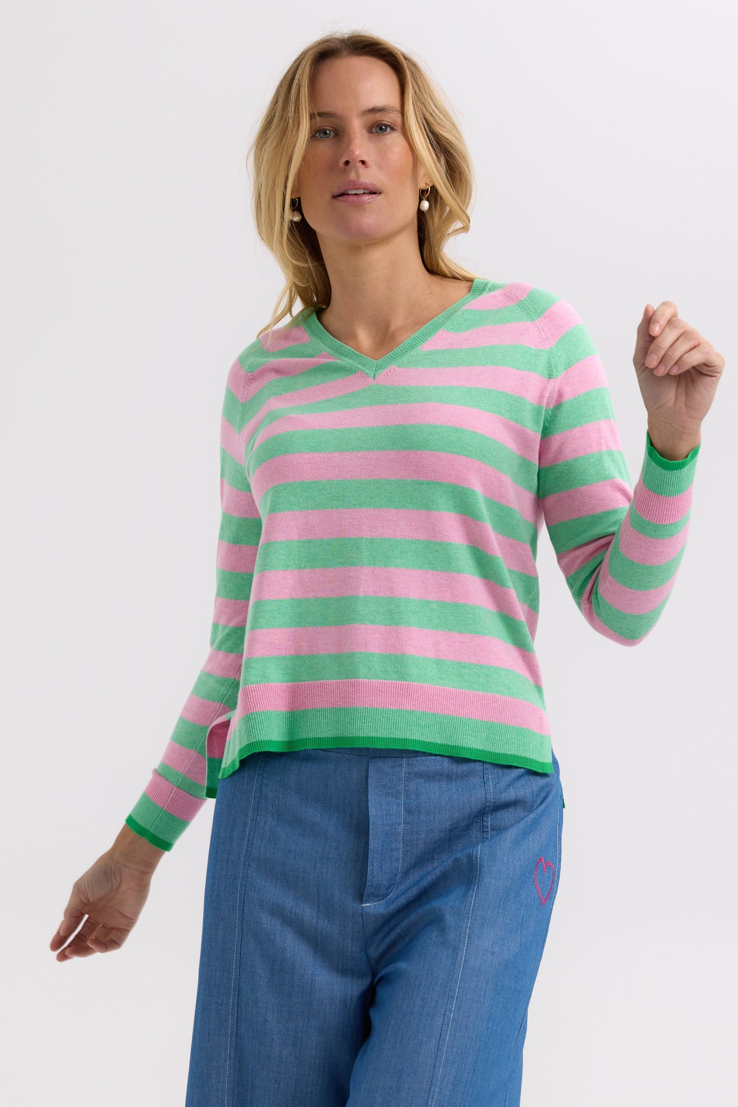 Woman wearing a pink and green striped sweater with blue pants on a white background