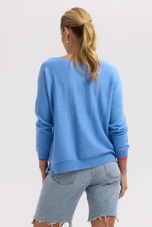 Person wearing a blue sweater and denim shorts on a plain background