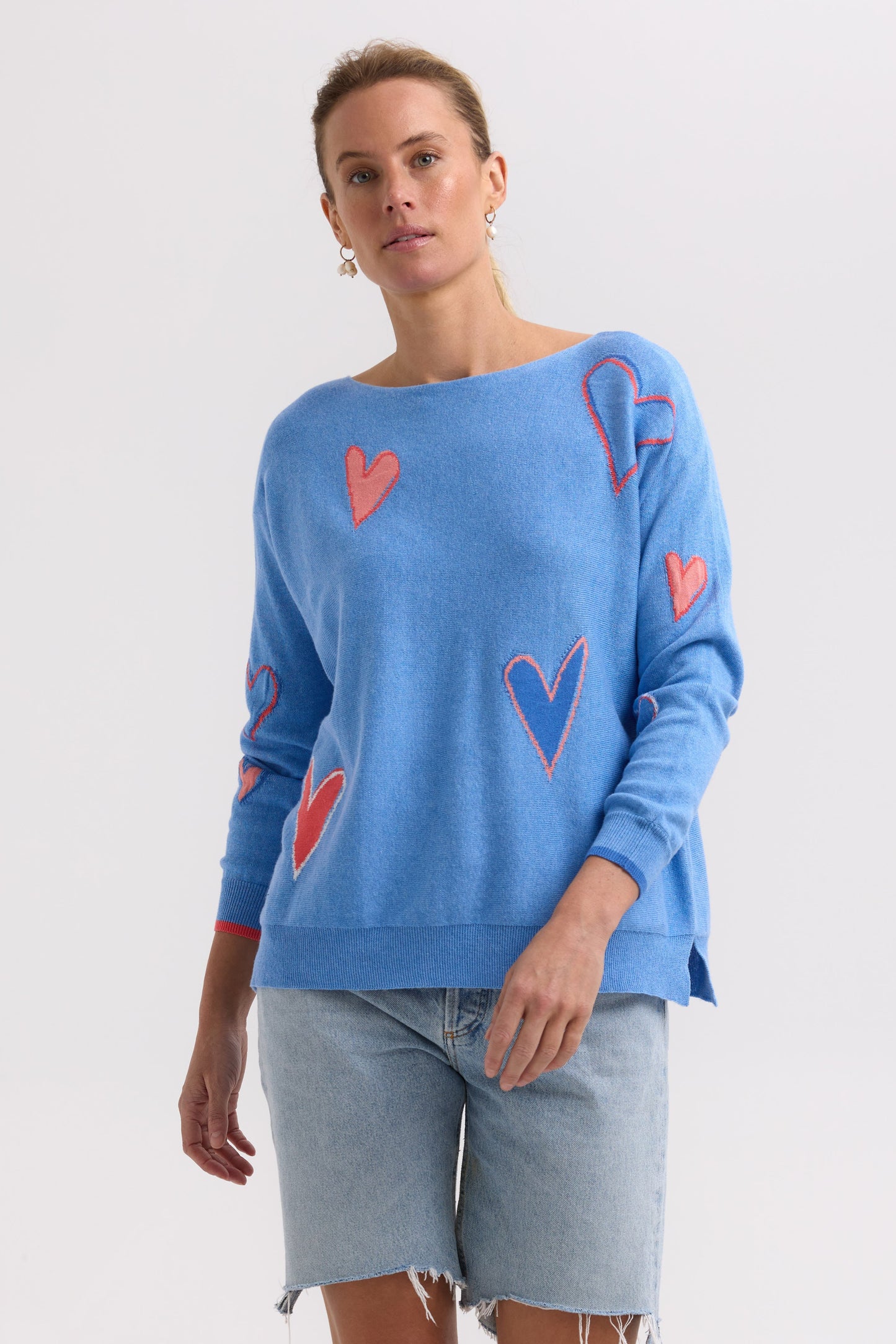 Woman wearing a blue sweater with red and pink heart patterns on a white background
