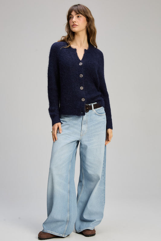 Woman wearing a navy cardigan and light blue jeans on a gray background