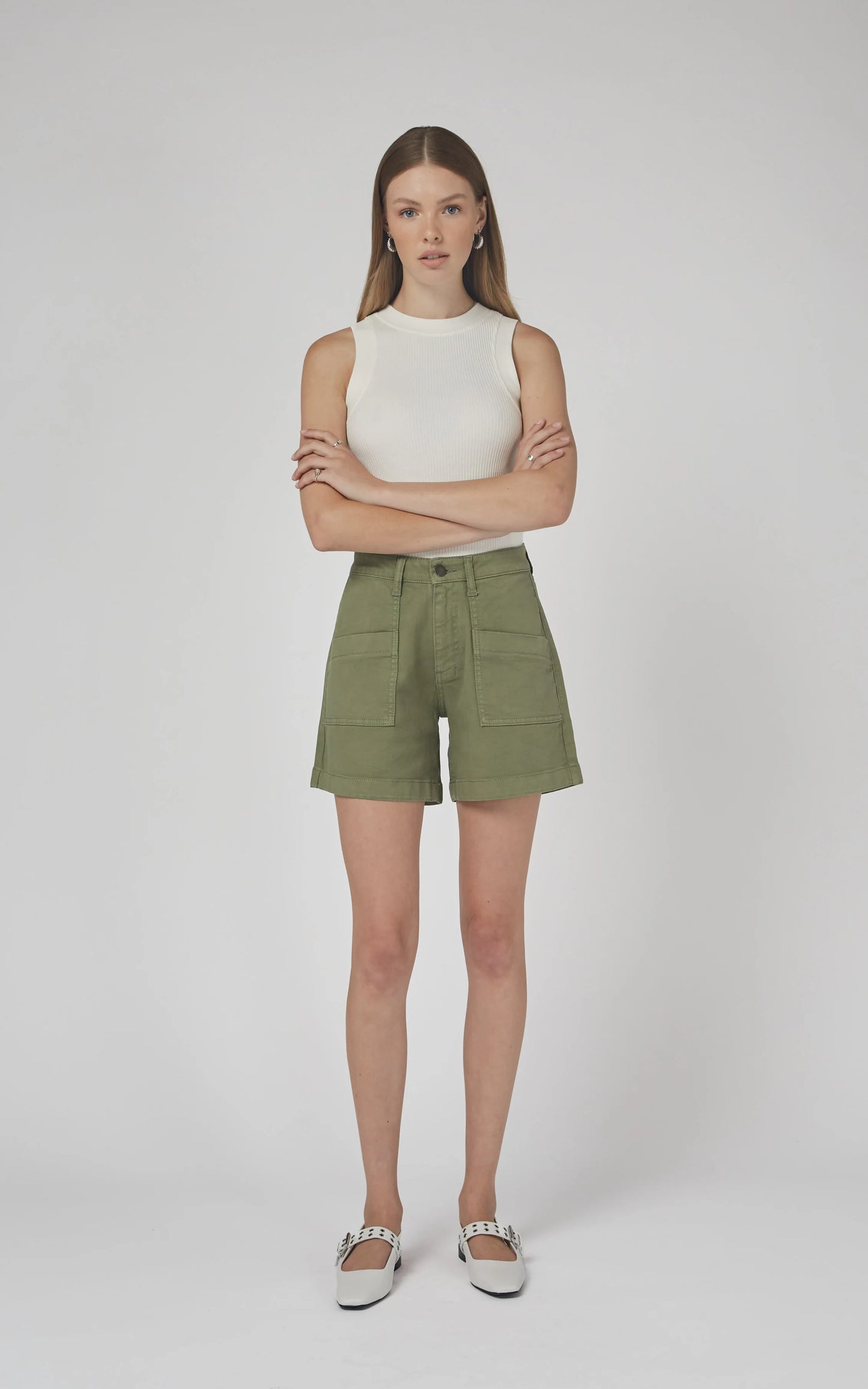 Woman wearing a white sleeveless top and green shorts on a plain background