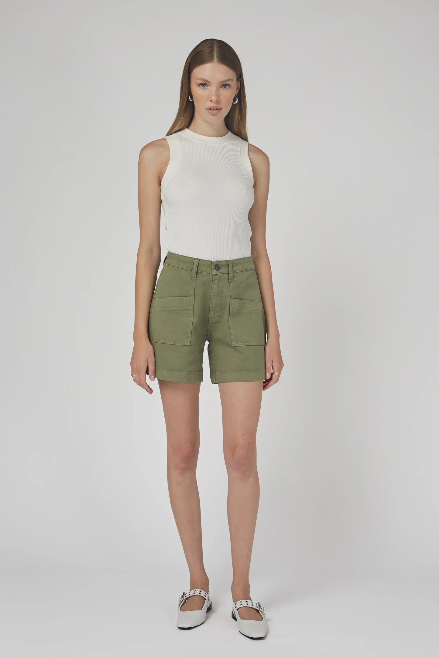 Woman wearing a white sleeveless top and green shorts on a plain background