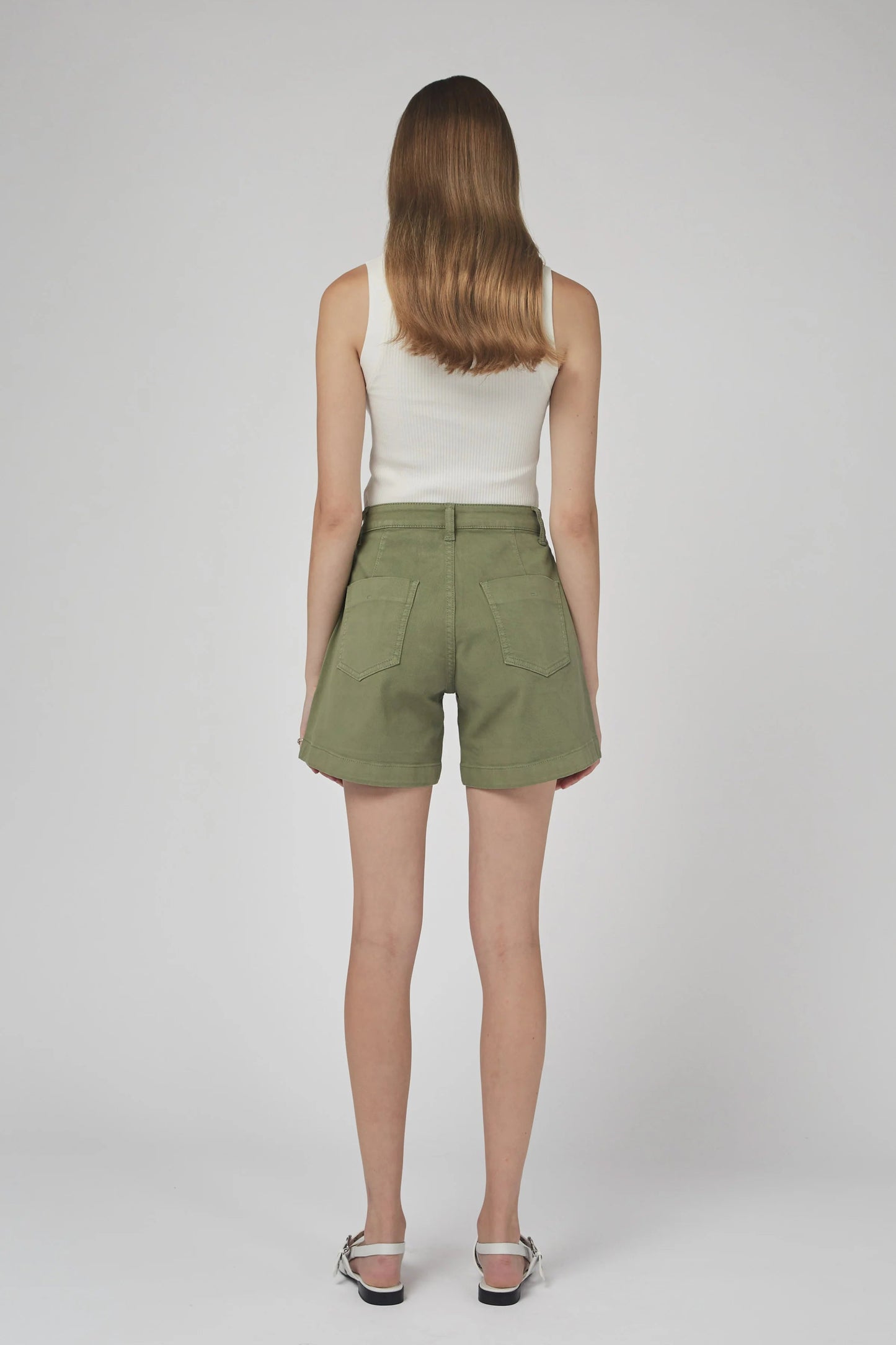 Woman wearing green shorts and a white top on a plain background