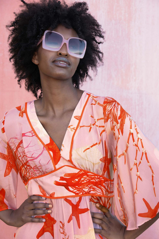 Woman wearing a pink and orange patterned kimono with sunglasses against a light pink background