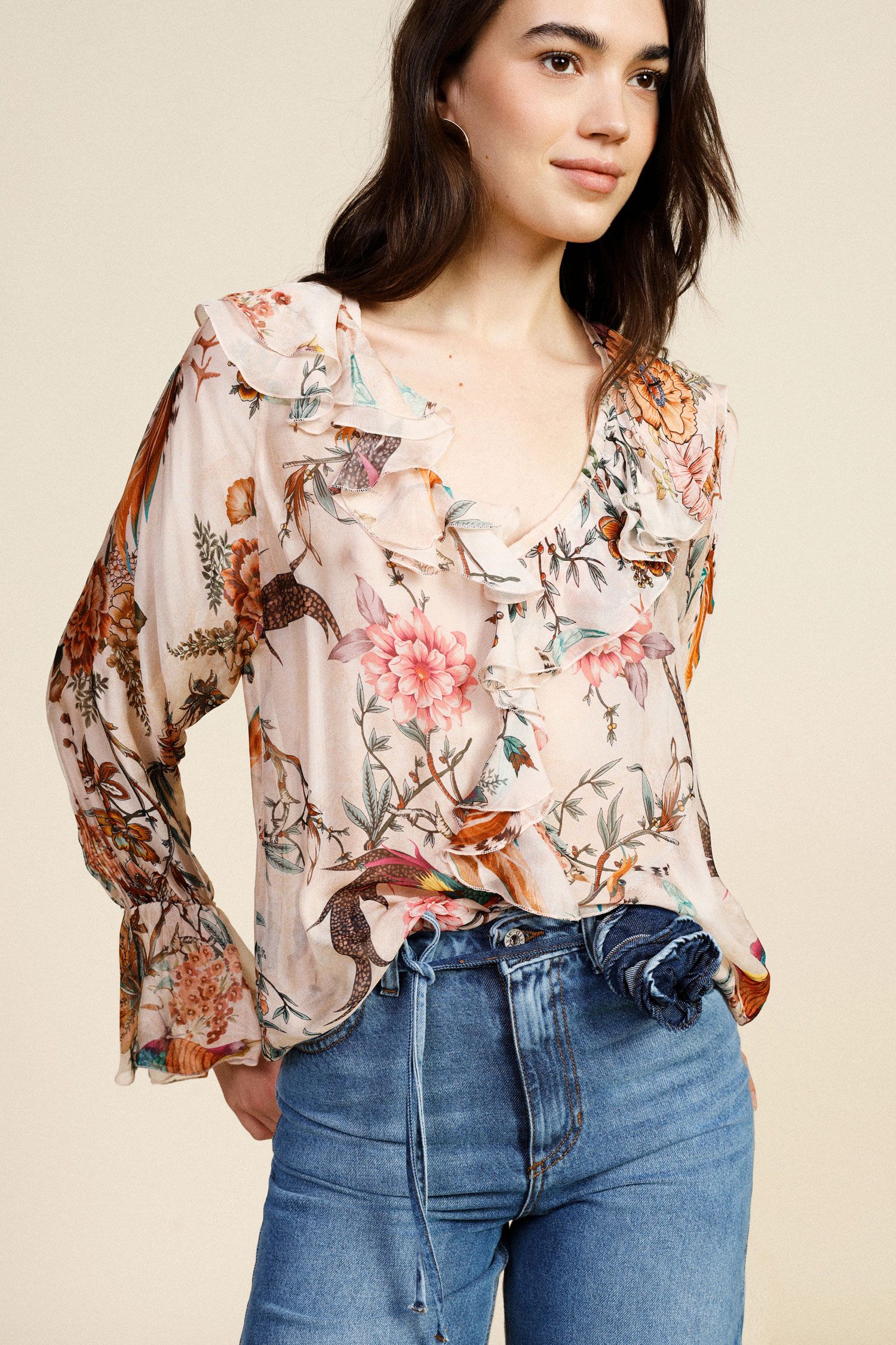Woman wearing a floral blouse and blue jeans against a beige background