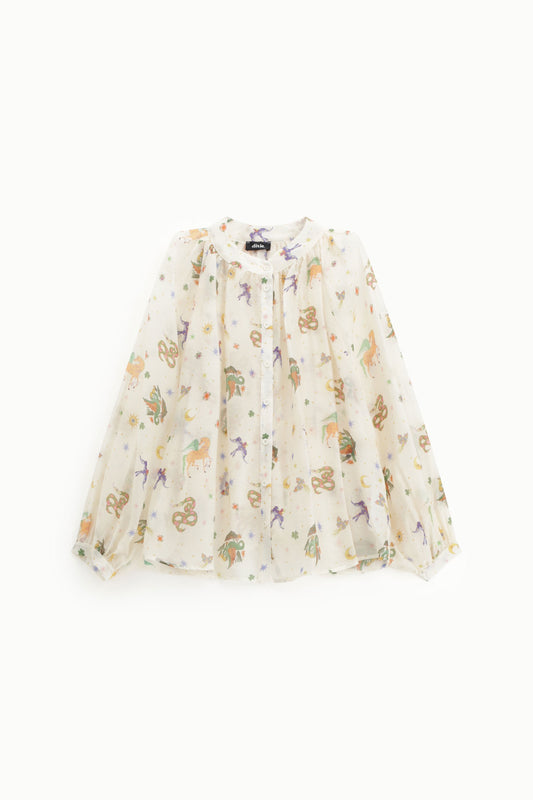 A long-sleeve, semi-sheer blouse in a warm cream or off-white color, decorated with a whimsical all-over print of colorful unicorns, stars, and moons. The blouse is displayed flat against a clean, solid white background.