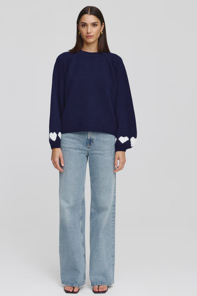 Woman wearing a navy sweater with white heart patterns and light blue jeans on a white background