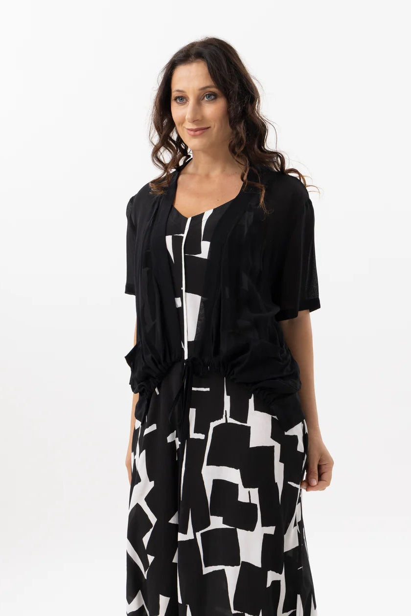 A woman modeling a black short-sleeve tunic top with a matching black and white geometric print skirt against a plain white studio background.