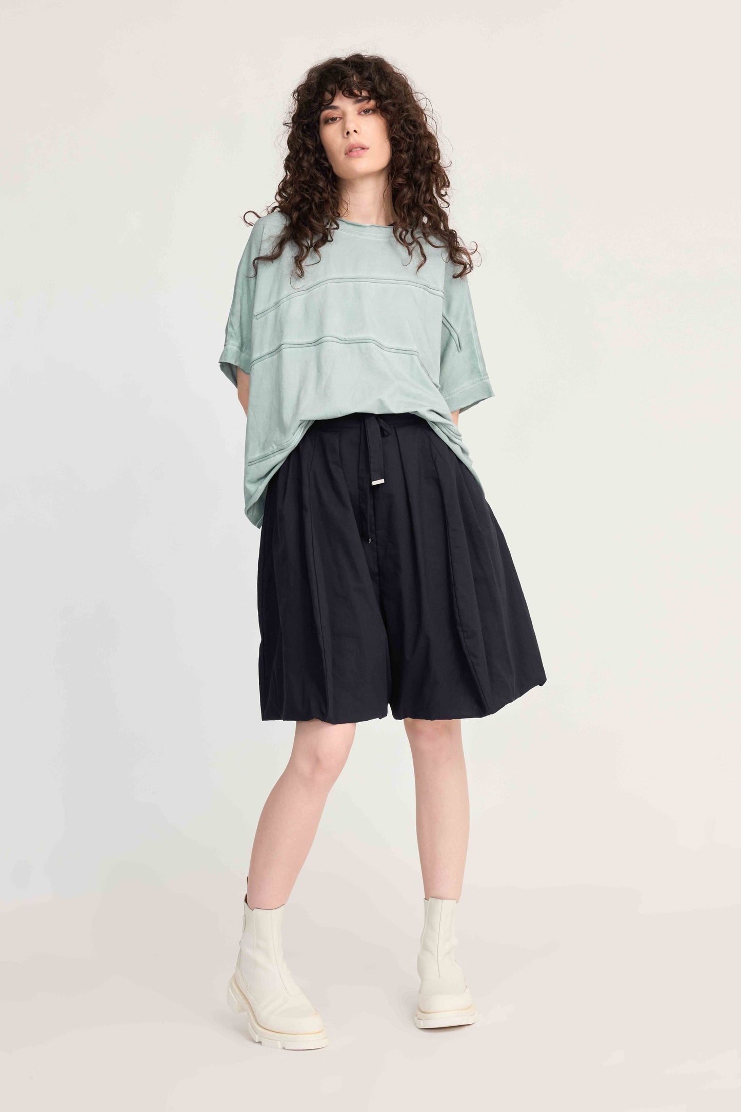 Person wearing a light green top and black shorts on a white background