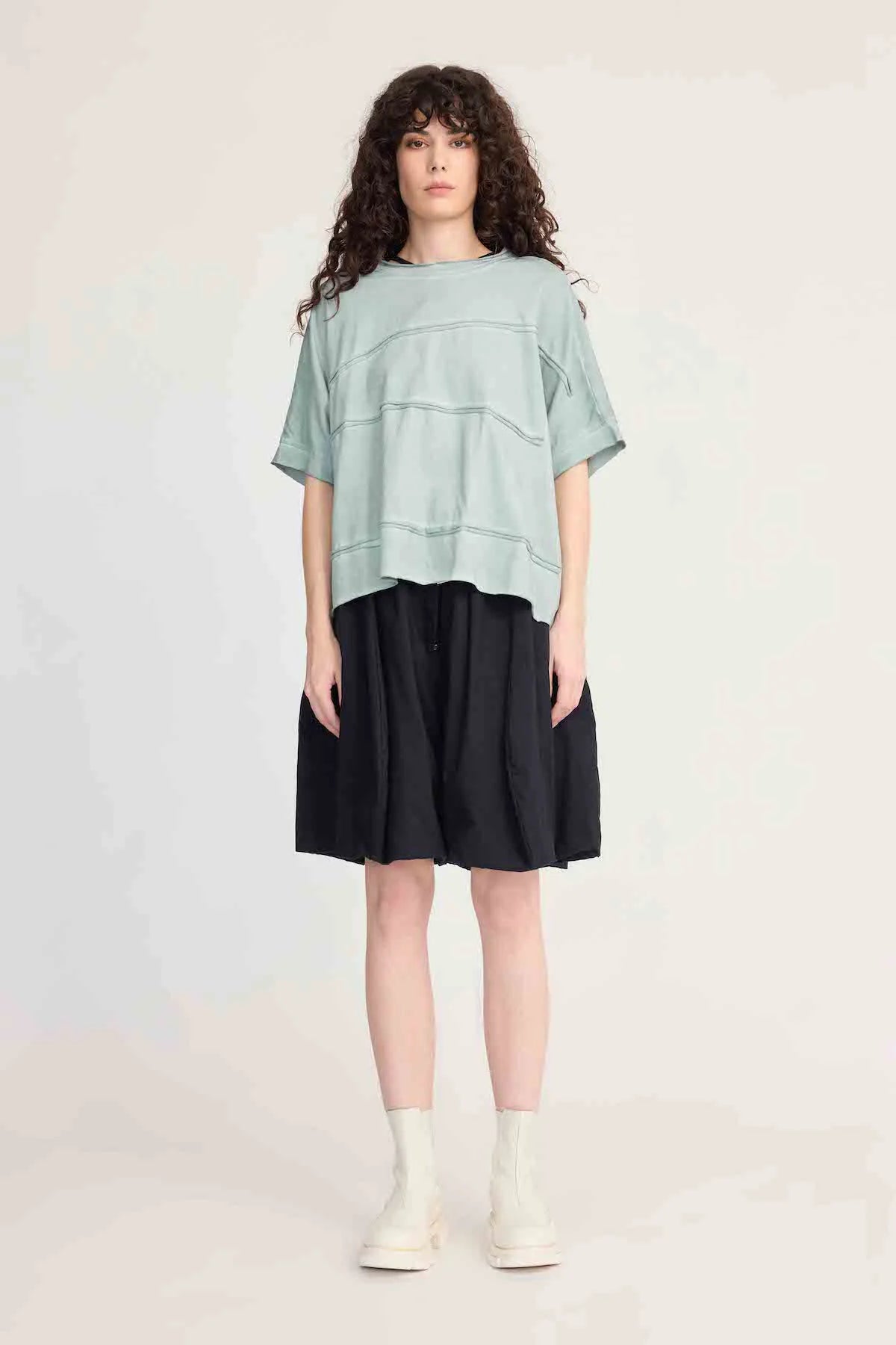 Woman wearing a layered outfit with a light green top and black skirt on a plain background