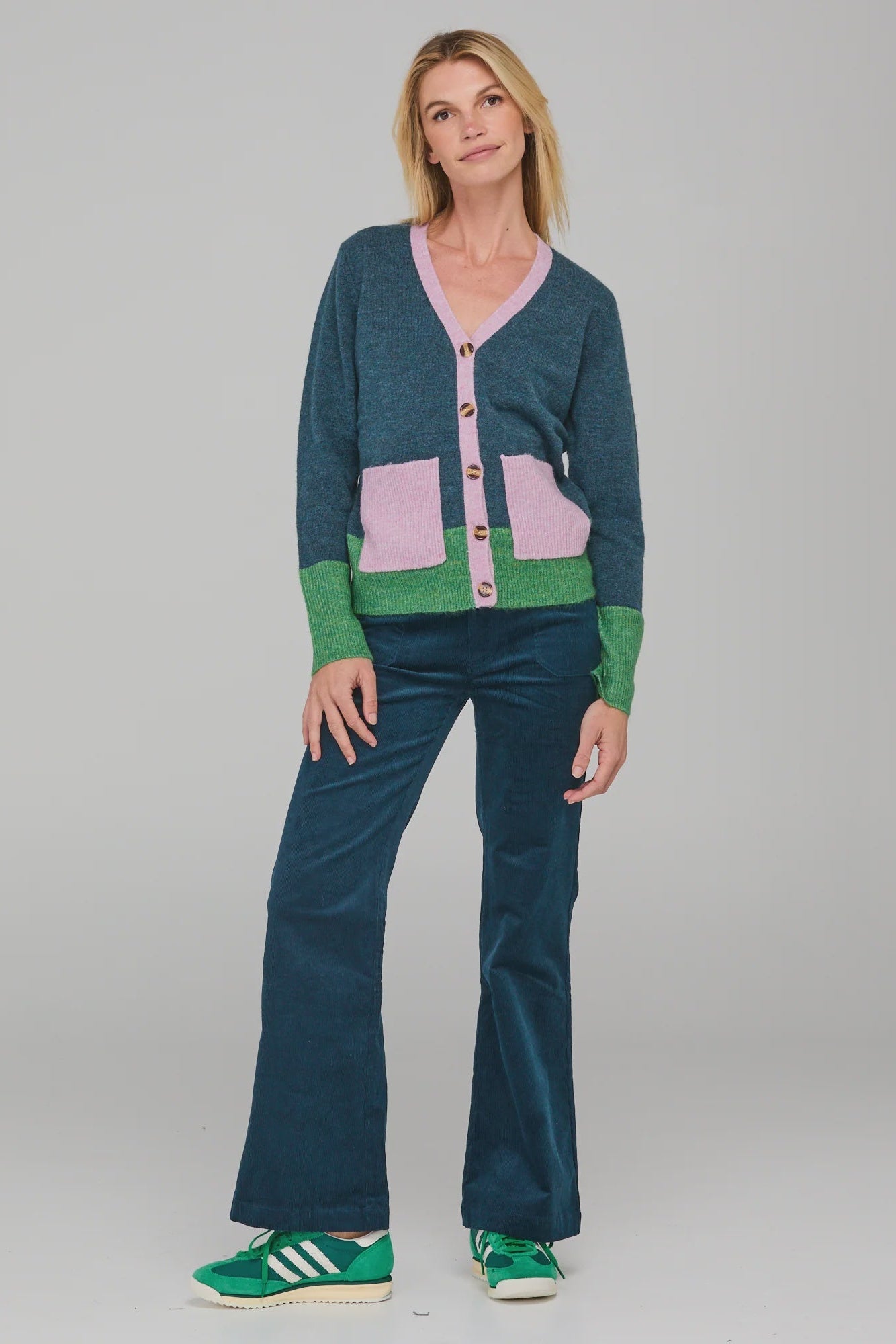 Woman wearing a colorful cardigan and pants with green sneakers on a gray background