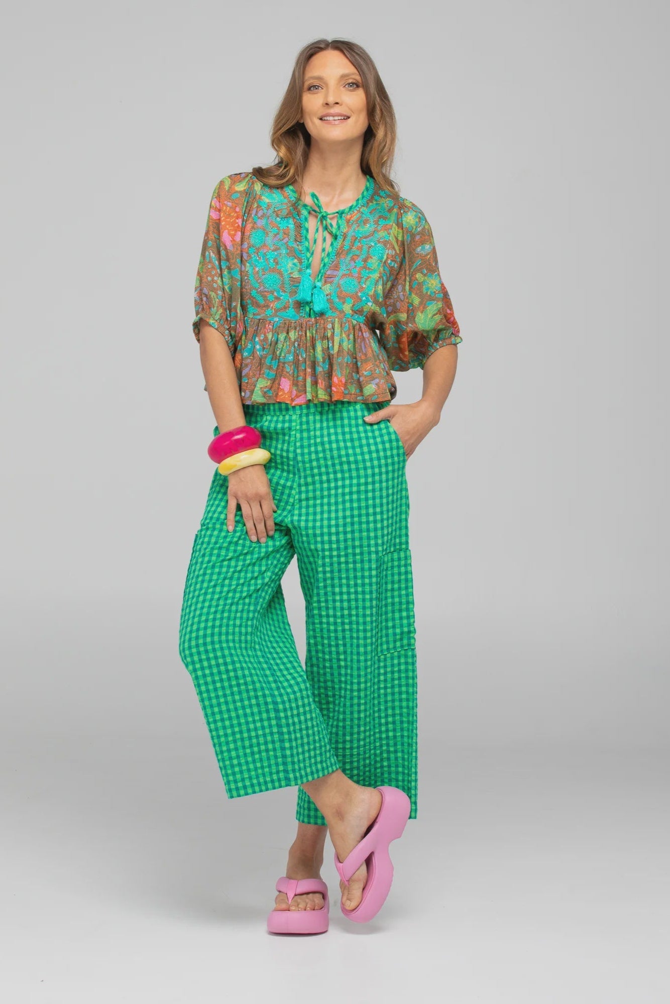 Woman wearing a colorful blouse and green checkered pants on a gray background