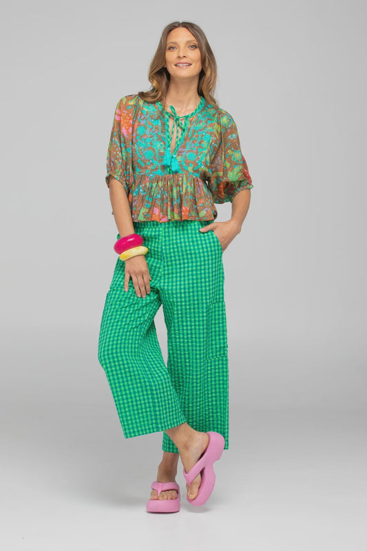 Woman wearing a colorful blouse and green checkered pants on a gray background