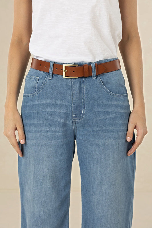 Person wearing blue jeans with a brown belt on a beige background