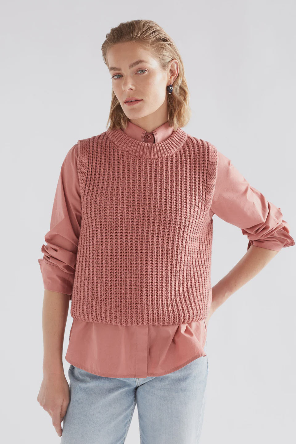Woman wearing a pink sweater over a pink shirt with light blue jeans on a white background