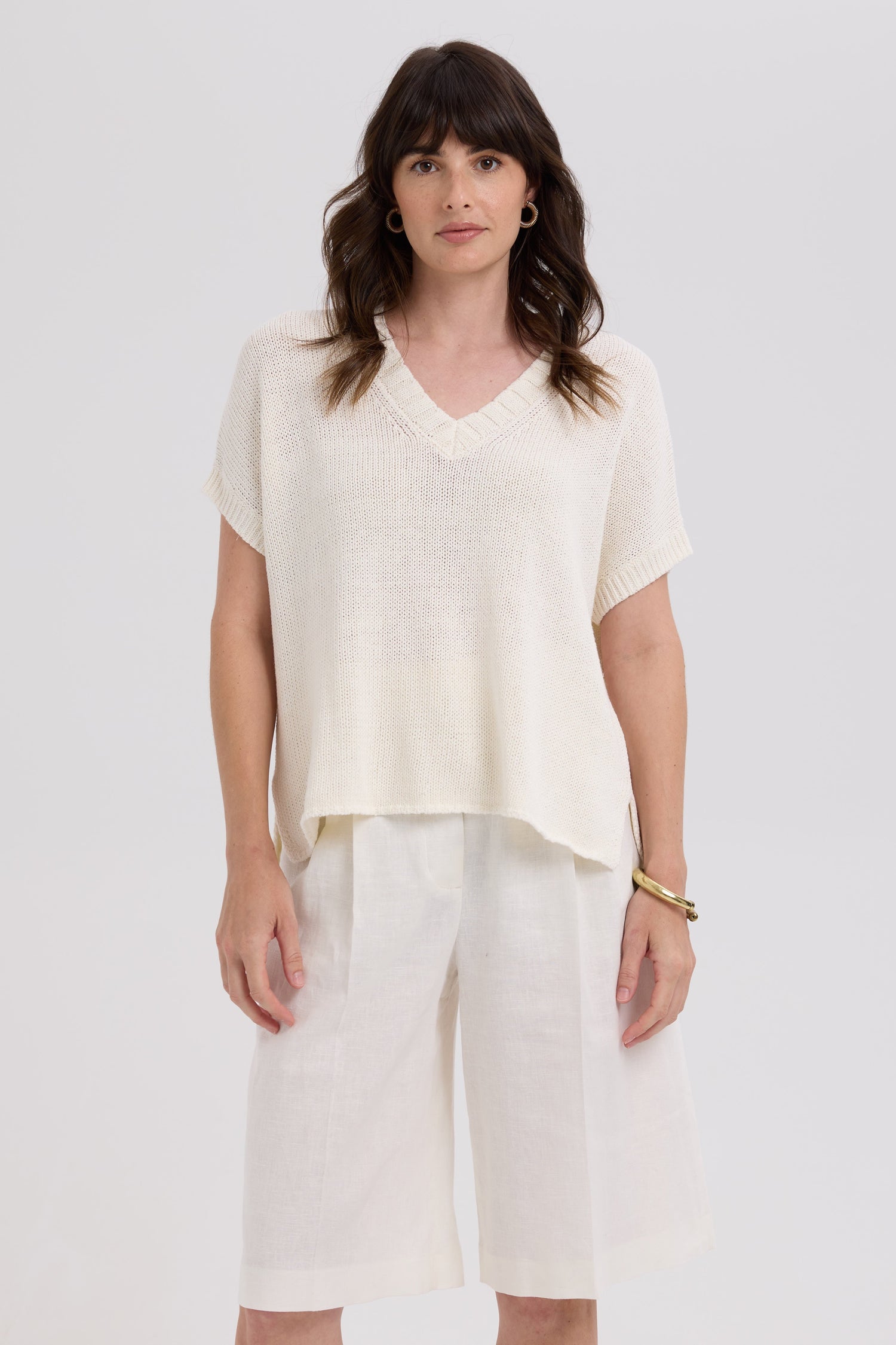 Woman wearing a white top and light-colored pants against a plain background