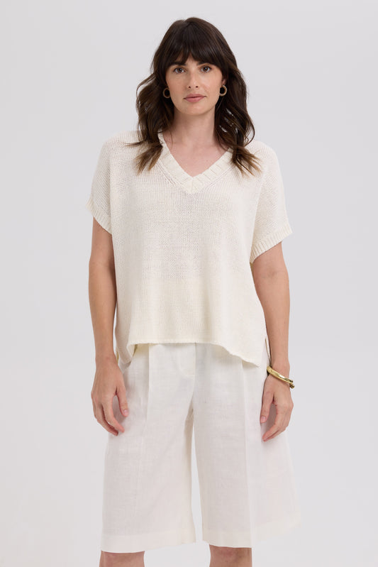 Woman wearing a white top and light-colored pants against a plain background