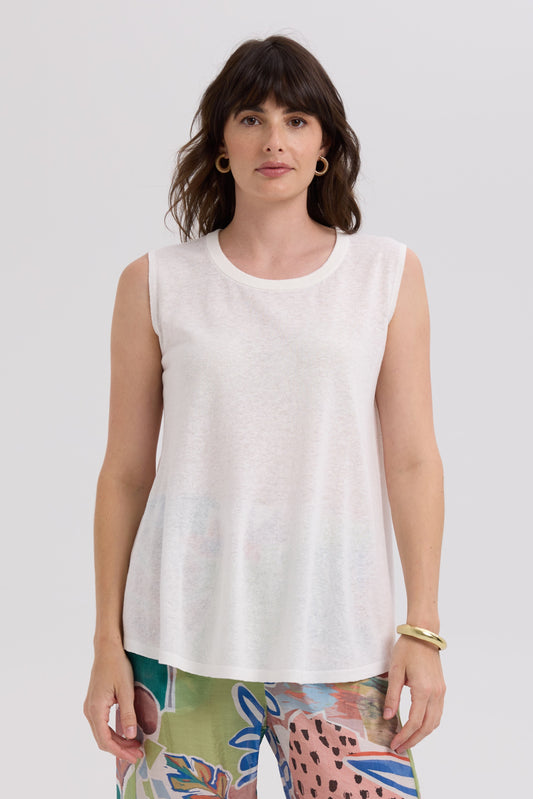 Woman wearing a white sleeveless top with colorful pants on a plain background