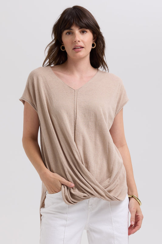 Woman wearing a beige top and white pants on a plain background