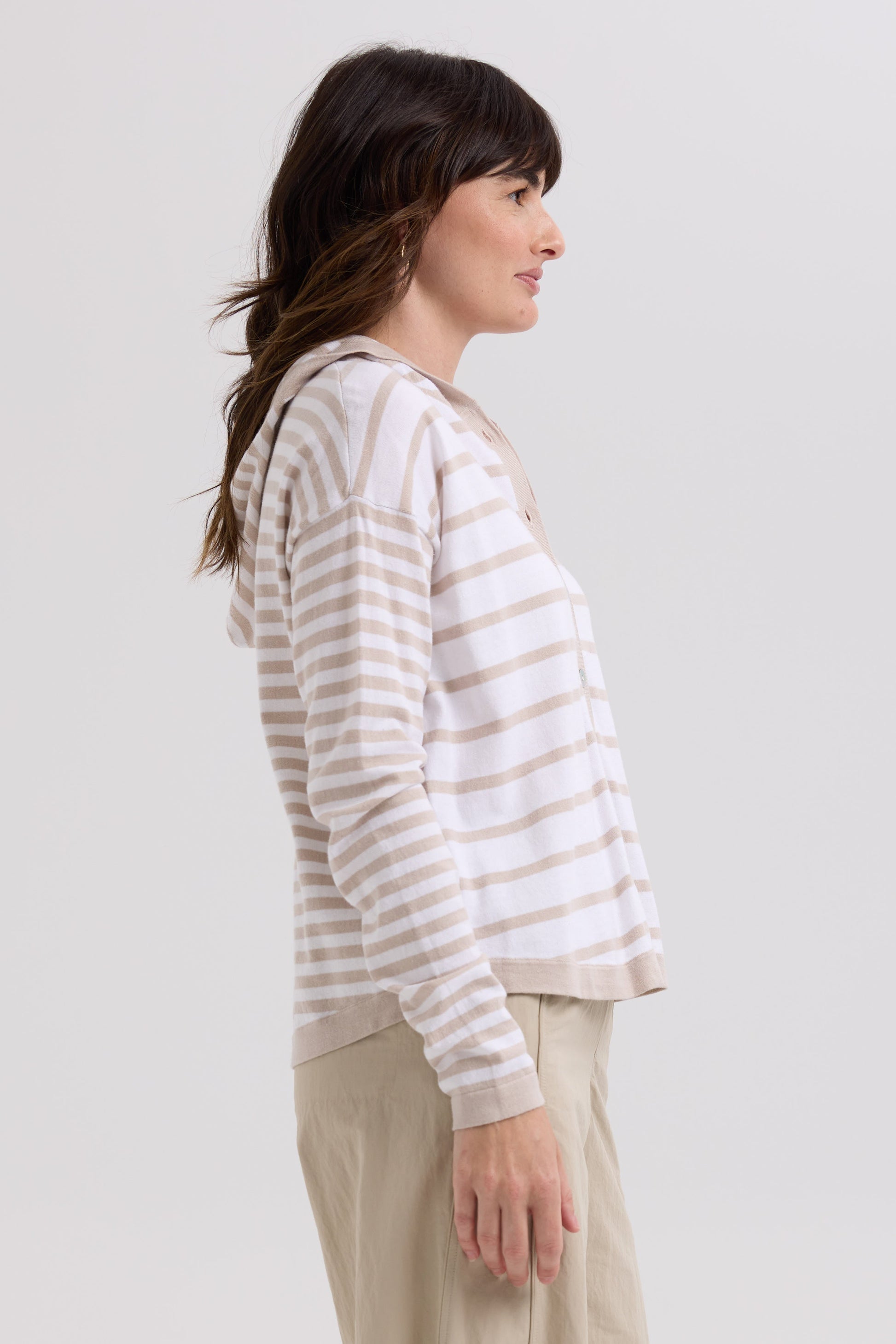Woman wearing a striped hoodie and beige pants on a plain background