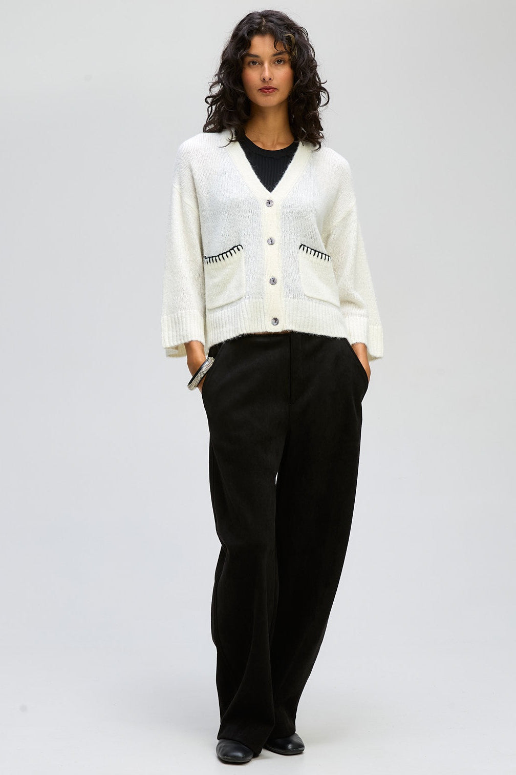 Woman wearing a white cardigan with black patterns and black pants on a white background