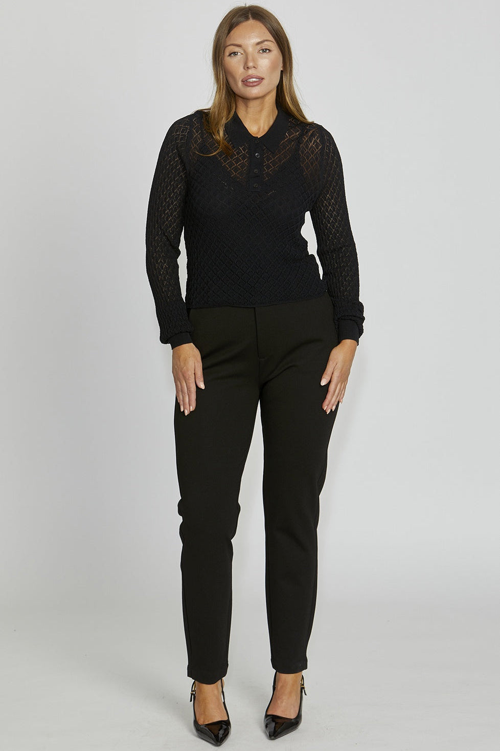 Woman wearing a black lace top and black pants on a gray background