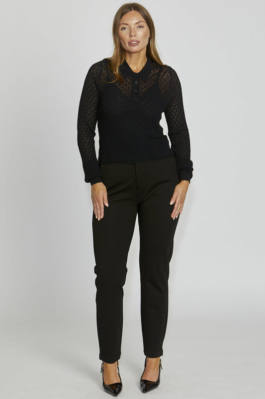 Woman wearing a black lace top and black pants on a gray background
