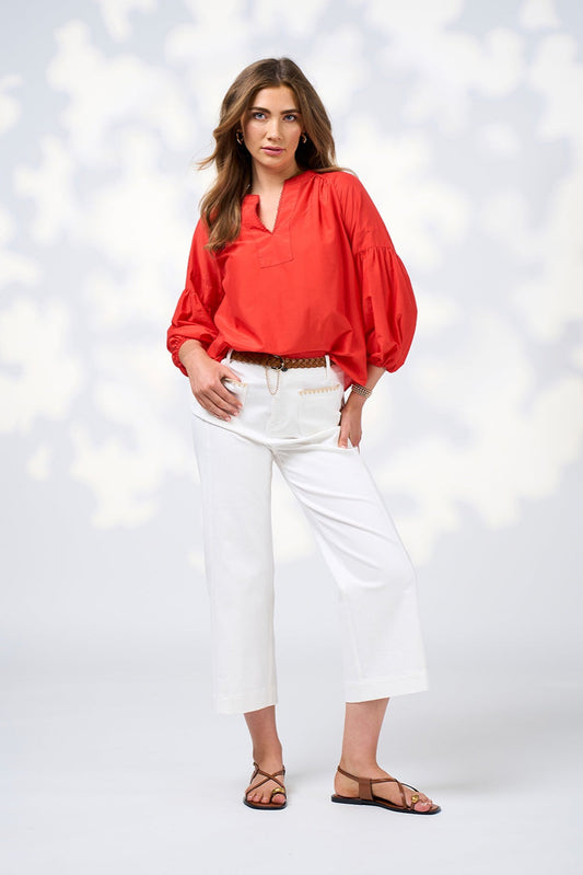 Woman wearing a red blouse and white pants against a light background