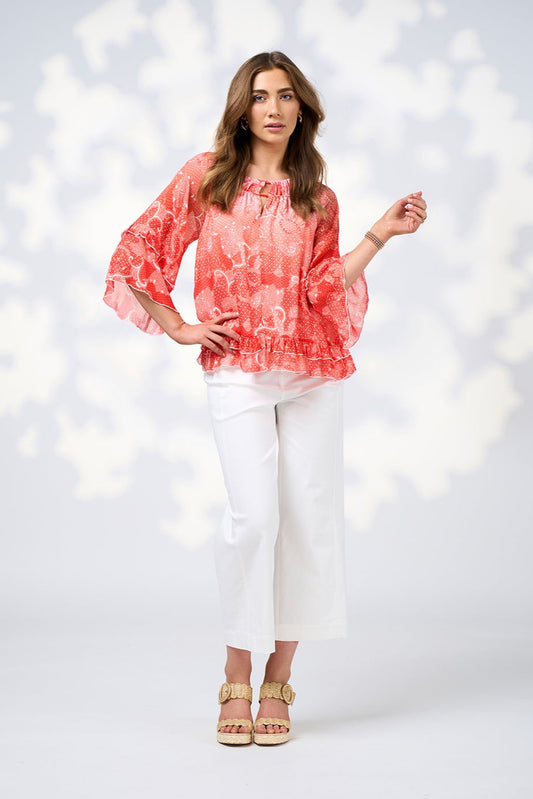 Woman wearing a coral patterned blouse and white pants against a light background